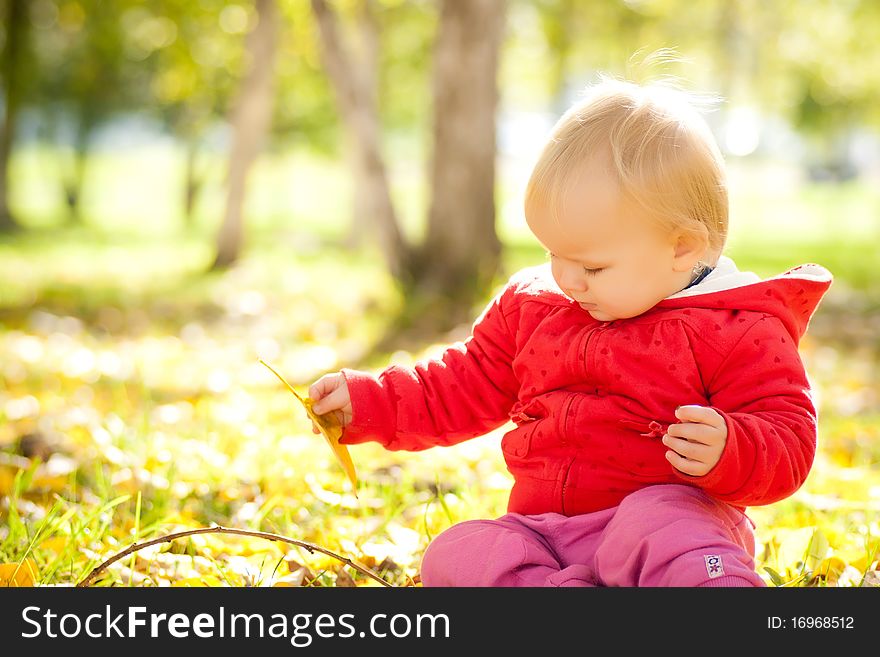 Young cheerful baby play with yellow leafs under trees in park