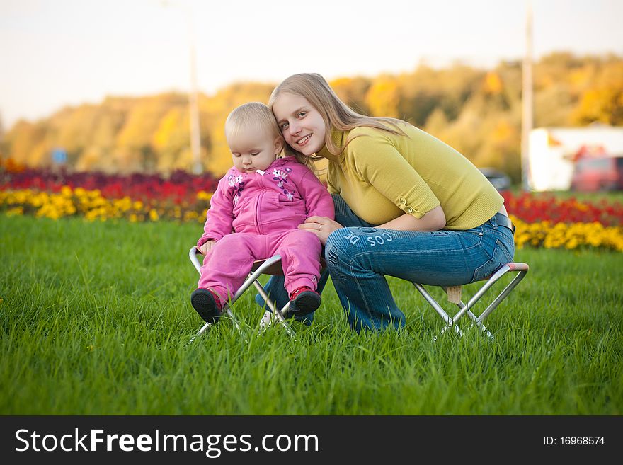 Young adorable woman and cute baby sitting on chairs in park