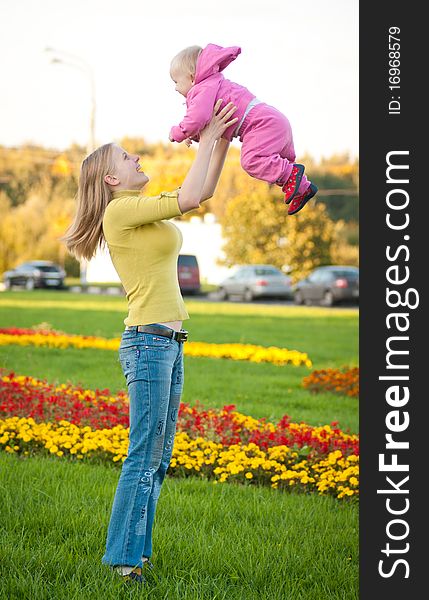 Young adorable woman stay on green grass and play with cute baby on hands in air. Young adorable woman stay on green grass and play with cute baby on hands in air