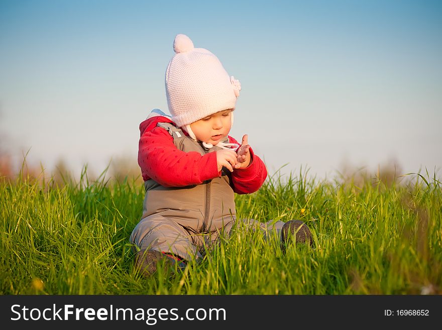 Young adorable baby sit on top of hill and look at hands