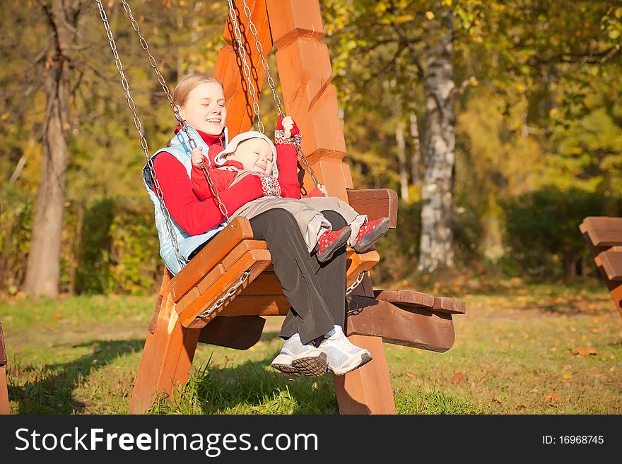 Young adorable mother swinging with dughter in autumn park