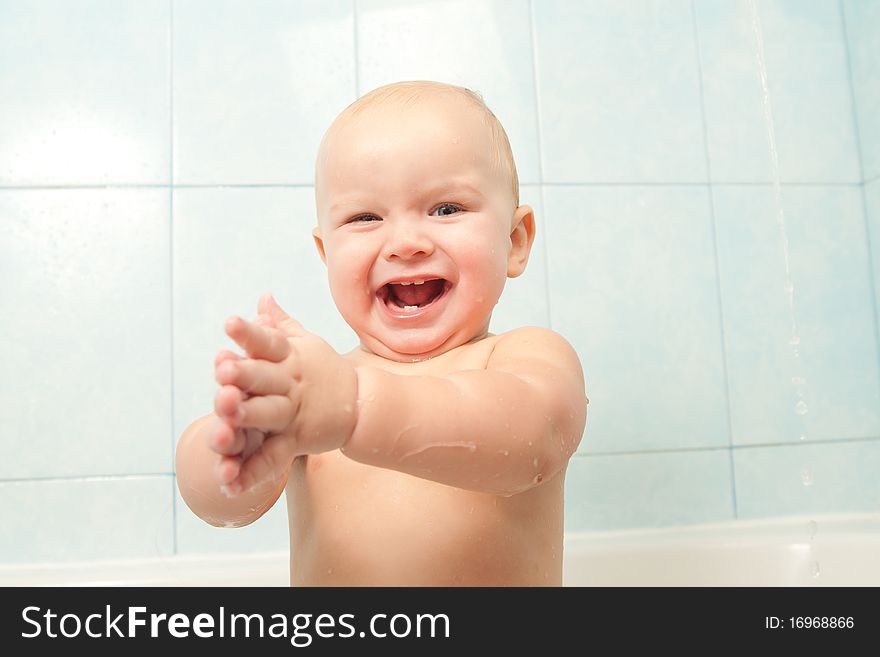 Cute cheerful baby slapping on the water in bath.