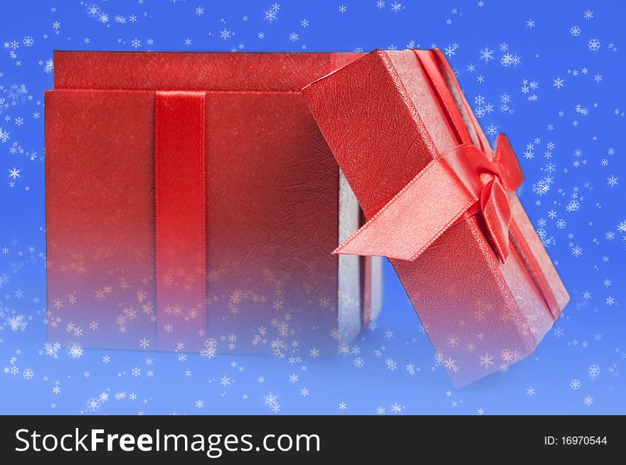 Christma spresent in form of a red box with ribbon melted with lue background with white snowflakes. Christma spresent in form of a red box with ribbon melted with lue background with white snowflakes