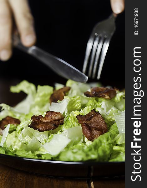Somebody eating a fresh caesar salad in a plate with big piece of bacon on it. Very shallow depth of field. Somebody eating a fresh caesar salad in a plate with big piece of bacon on it. Very shallow depth of field.