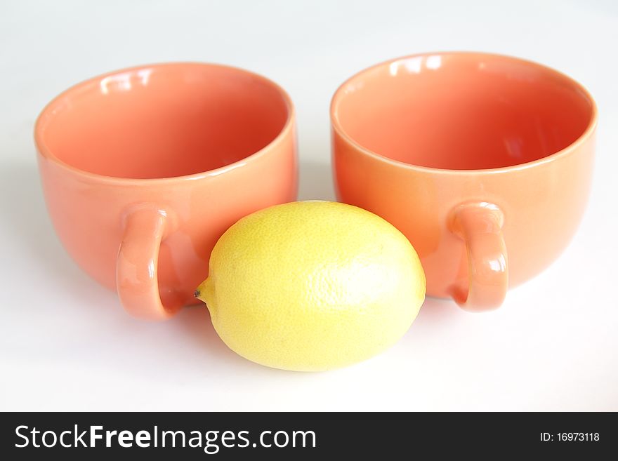 Two orange empty tea cups with whole lemon on white background. Two orange empty tea cups with whole lemon on white background
