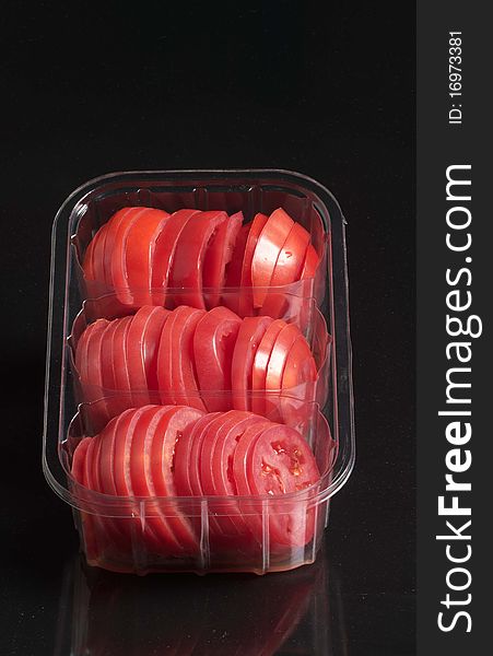 Tomato slices in plastic container on black background