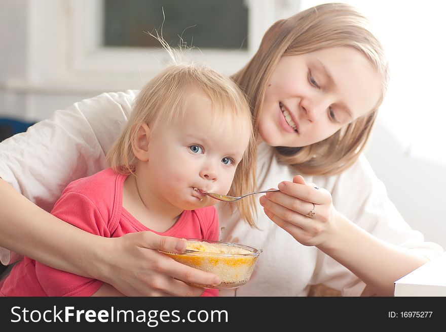 Young mother feeding daughter with porridge