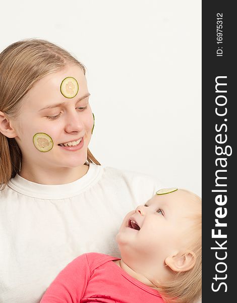 Young adorable mother with daughter play with sliced cucumbers on faces. Young adorable mother with daughter play with sliced cucumbers on faces