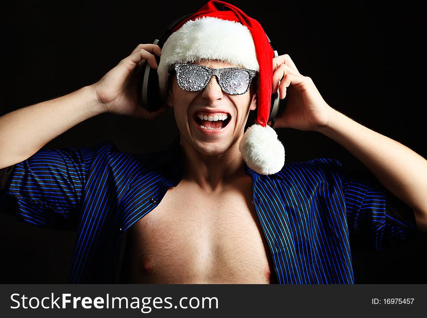 Portrait of a funny young man in Santa Claus hat and headphones. Christmas. Portrait of a funny young man in Santa Claus hat and headphones. Christmas.