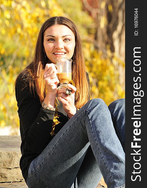 Happy young woman drinking coffee on a bright fall day