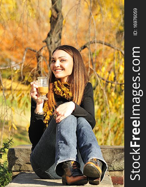 Happy young woman drinking coffee on a bright fall day