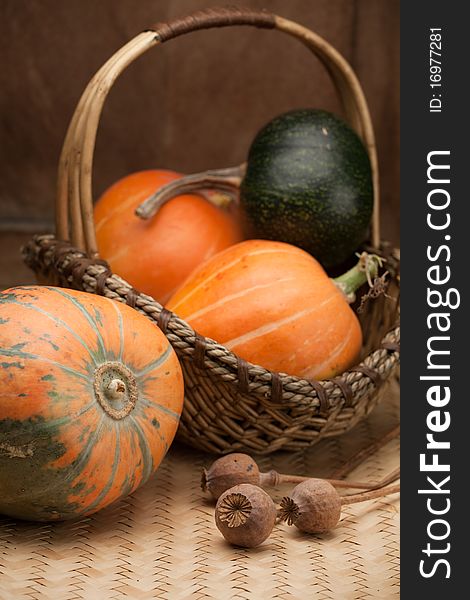 Ripe pumpkins in woven basket and poppy on table