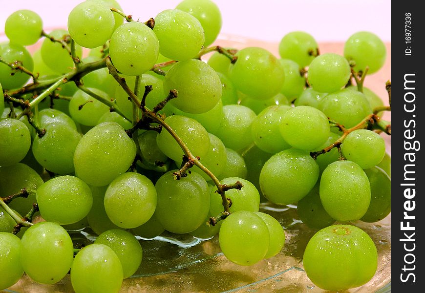 Clusters of green grapes, sitting on a glass plate, sitting on a wooden cutting board with a white background.