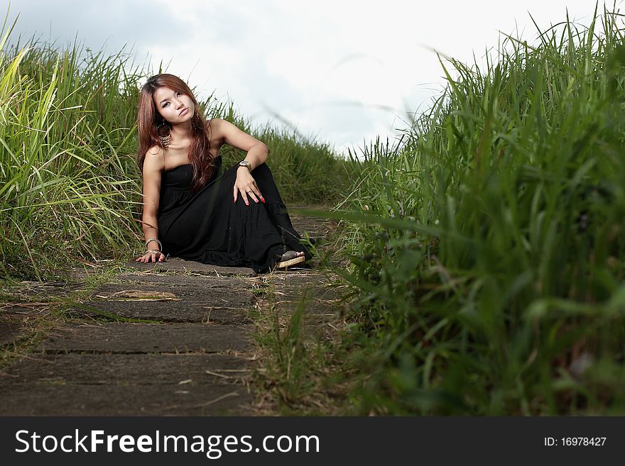 Asian woman sitting outdoor in the meadow with black dress. Asian woman sitting outdoor in the meadow with black dress