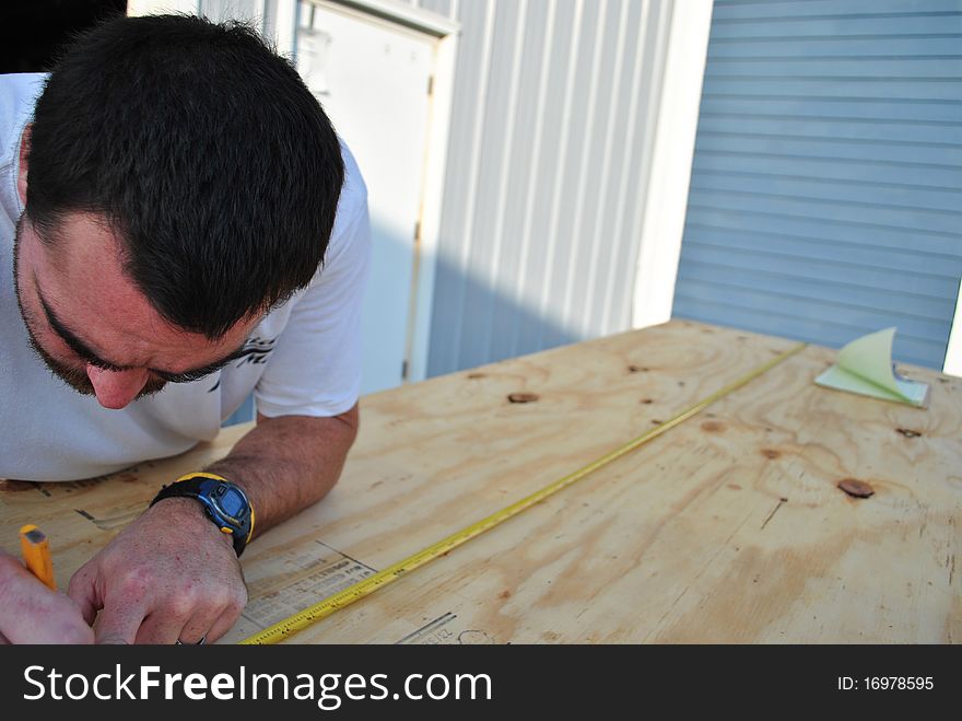 A man taking measurements on a sheet of plywood. A man taking measurements on a sheet of plywood.