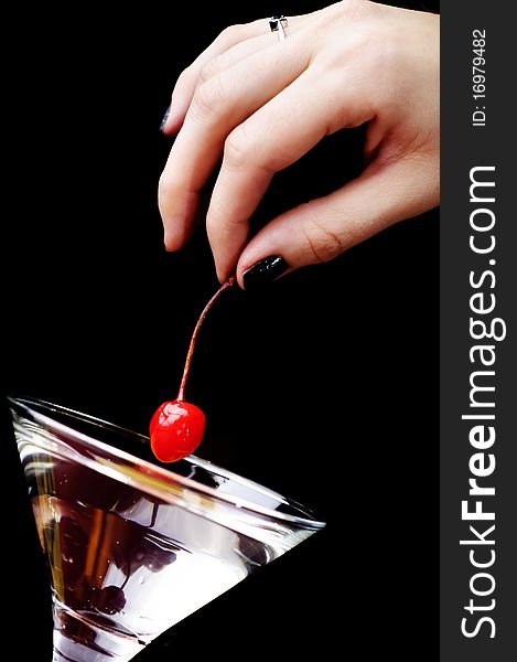 The hand putting the red cherry to the martini glass. The hand putting the red cherry to the martini glass