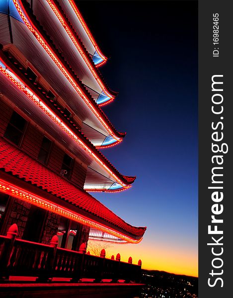 A view of a Chinese pagoda at dusk with the sunsetting over a city in the background. A view of a Chinese pagoda at dusk with the sunsetting over a city in the background