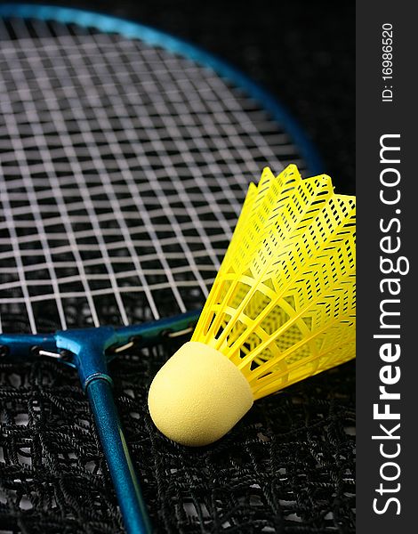 A bright yellow badminton shuttlecock and a blue racquet laying on a net. A bright yellow badminton shuttlecock and a blue racquet laying on a net.