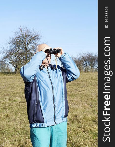 Senior man looking at with binoculars in the nature in Autumn. Senior man looking at with binoculars in the nature in Autumn