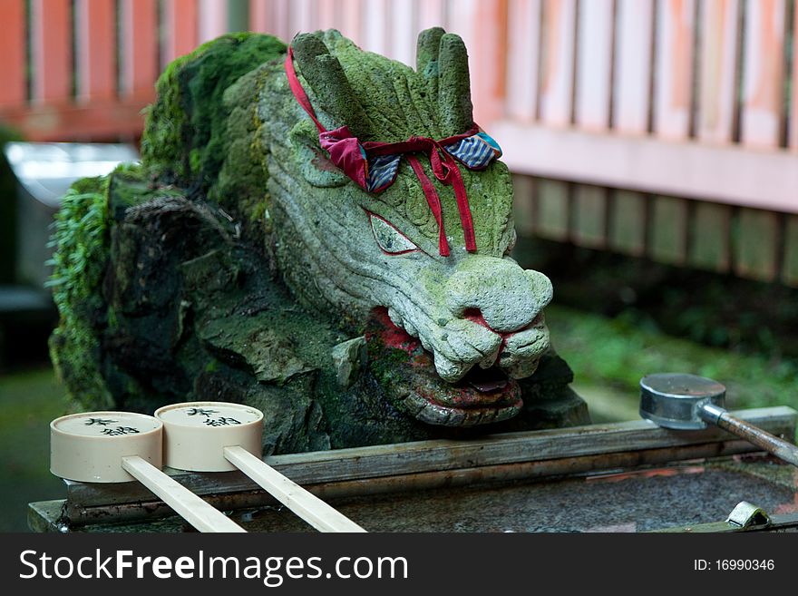 A stone dragon covered in moss sits next to water purification at entrance of Japanese shrine. A stone dragon covered in moss sits next to water purification at entrance of Japanese shrine
