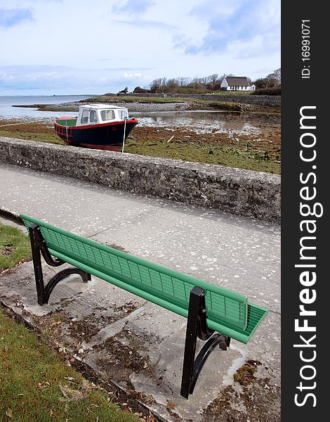 A green metal bech with a view of an old boat in a bay in ireland. A green metal bech with a view of an old boat in a bay in ireland