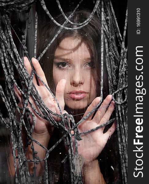 Portrait of young girl looking through wet window and textile net