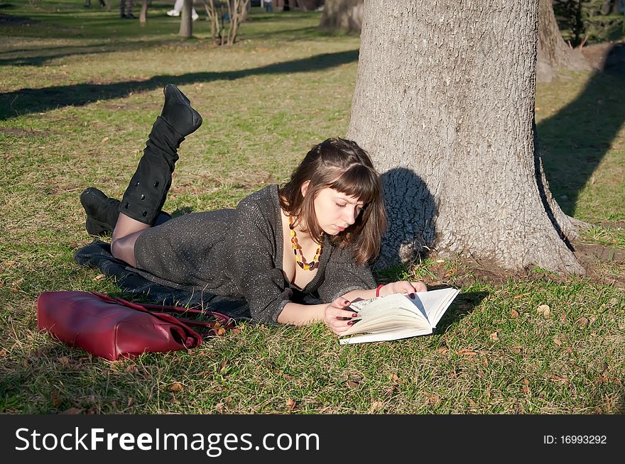 Girl reading while lying in a park on the grass