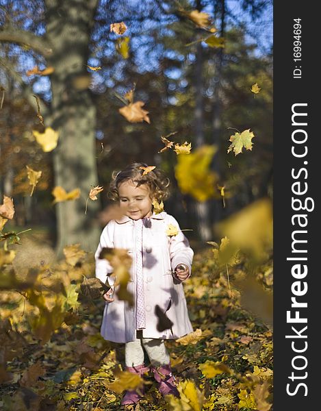 Portrait with little girl in autumn in the park with leaves fallen down on her