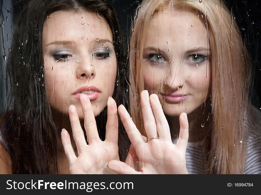 Two young girls behind wet window. Two young girls behind wet window