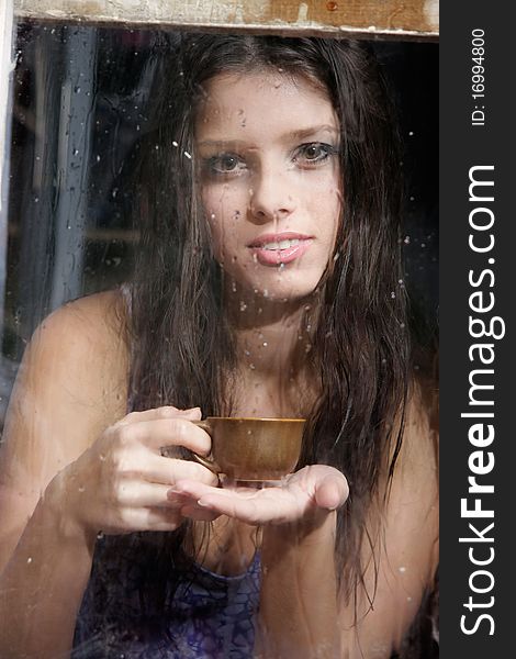 Girl with cup of tea behind wet window