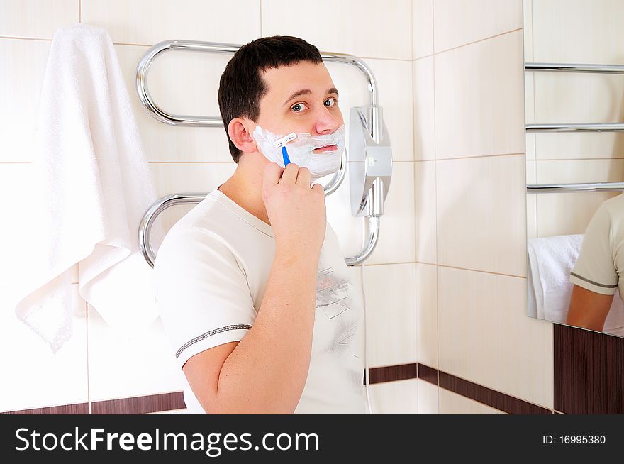 Young man shaving in his bathroom standing in front of a mirror