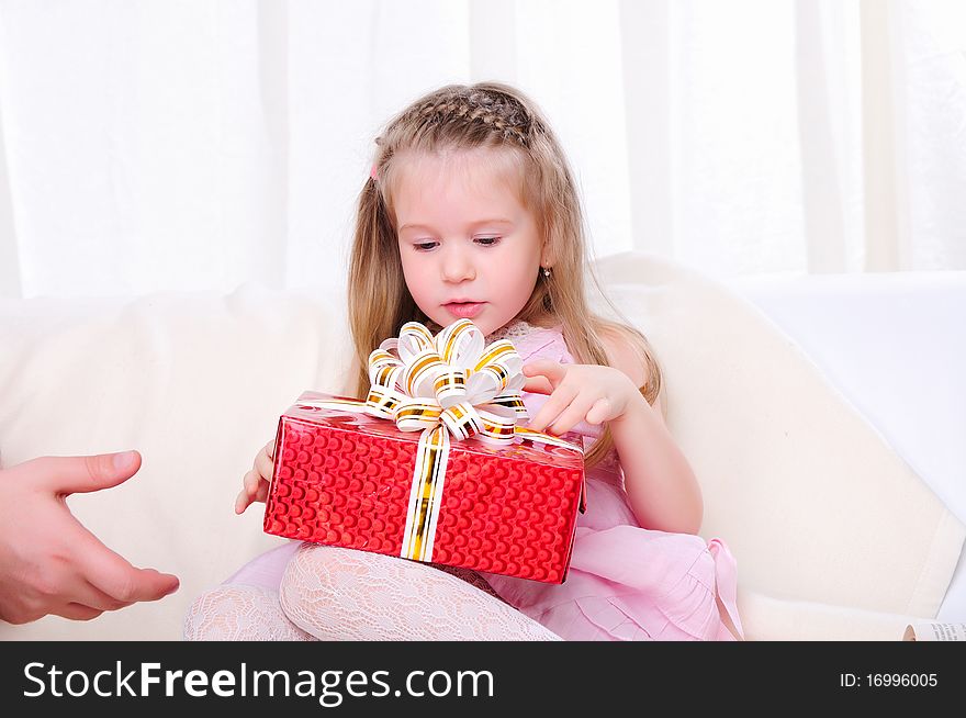 A little girl give a holiday gift in red box with white ribbon.