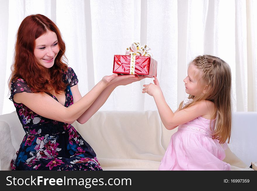 Little girl mom gives a holiday gift in red box with white ribbon.