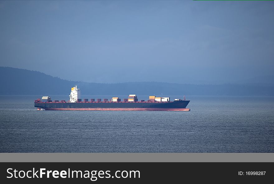 A partially loaded red and black container ship on the ocean blue.