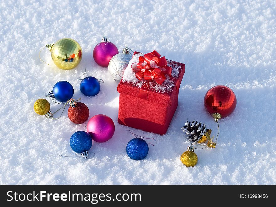 Red gift box on snow with christmas balls