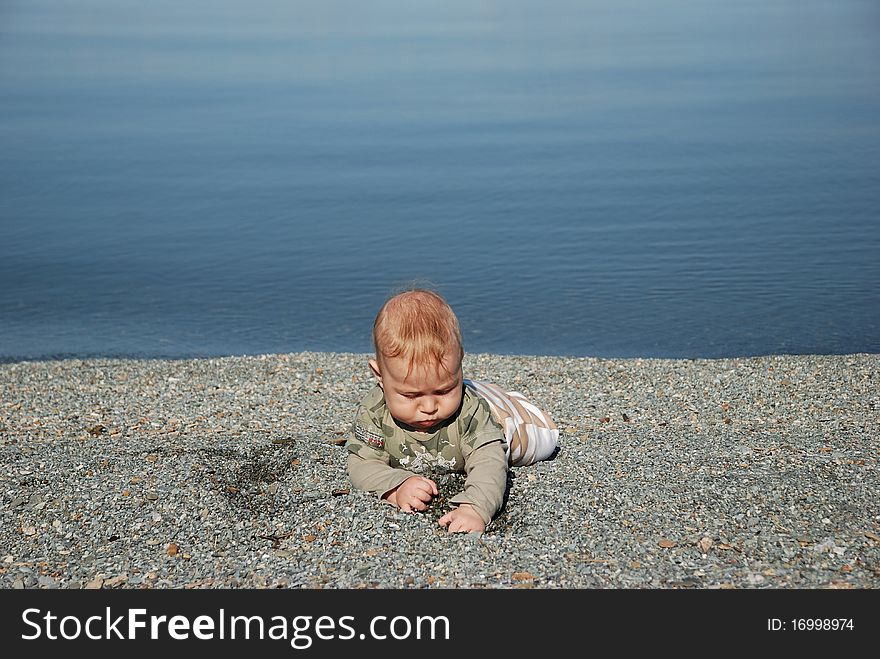 The kid digs a hole in sand on the bank of lake. The kid digs a hole in sand on the bank of lake