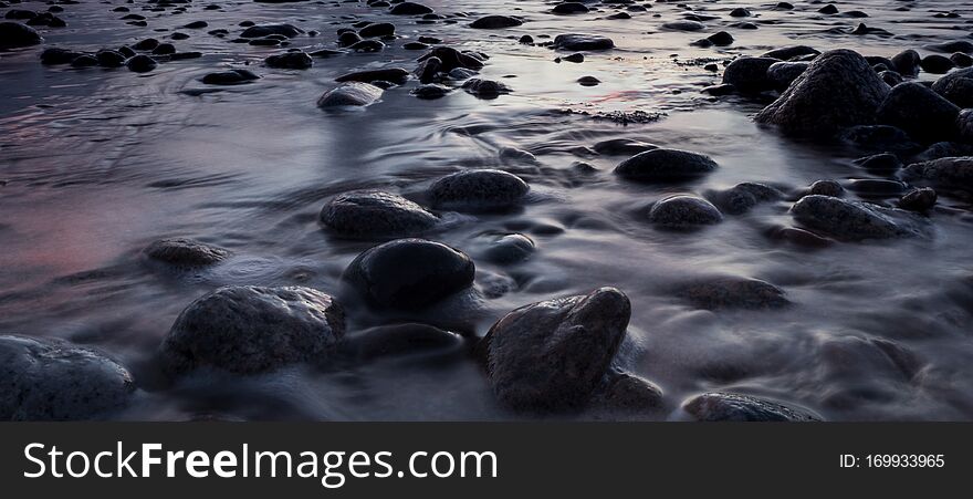 Water washes over pebbles along the coast in a long exposure shot of the tauranga harbour
