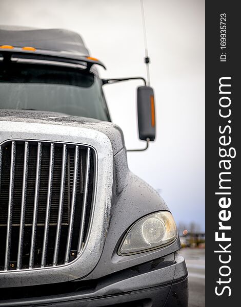 Front of dark gray big rig semi truck with efficient eco-friendly diesel engine and chrome grille with rain drops standing on the industrial parking lot. Front of dark gray big rig semi truck with efficient eco-friendly diesel engine and chrome grille with rain drops standing on the industrial parking lot.