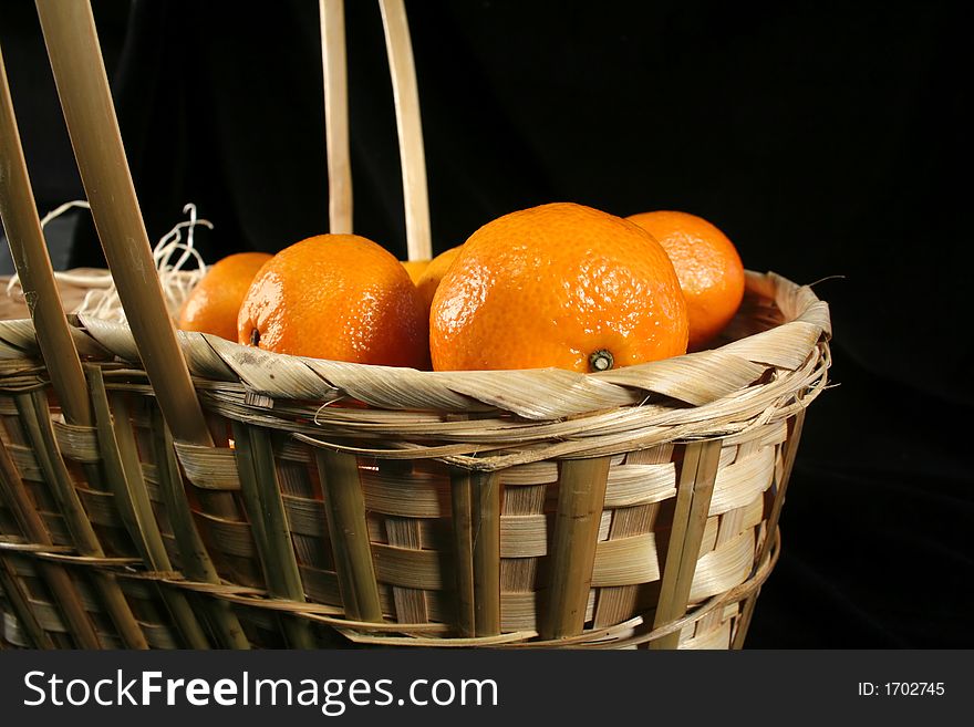 Clementines imported from Spain in a basket on a black background.  These are also knows as Satsumas and are grown in southern Louisiana.