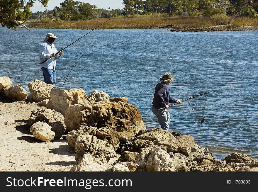 Two men catch fish with poles and nets on the riverbank. Two men catch fish with poles and nets on the riverbank.