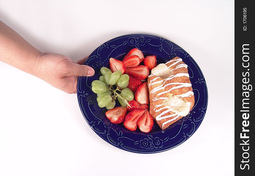 Pastry, grapes and strawberry on a blue plate holding by hand