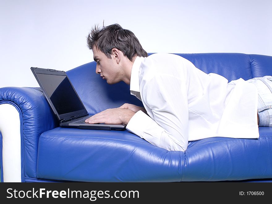 Young man comfortably sitting in a sofa using a laptop. Young man comfortably sitting in a sofa using a laptop