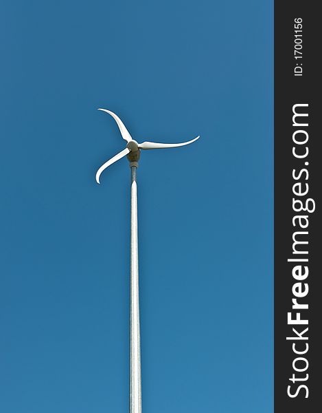 Alternative energy - A windmill with curved vanes spins on top of a tall pole with a deep blue sky in the background. Alternative energy - A windmill with curved vanes spins on top of a tall pole with a deep blue sky in the background.
