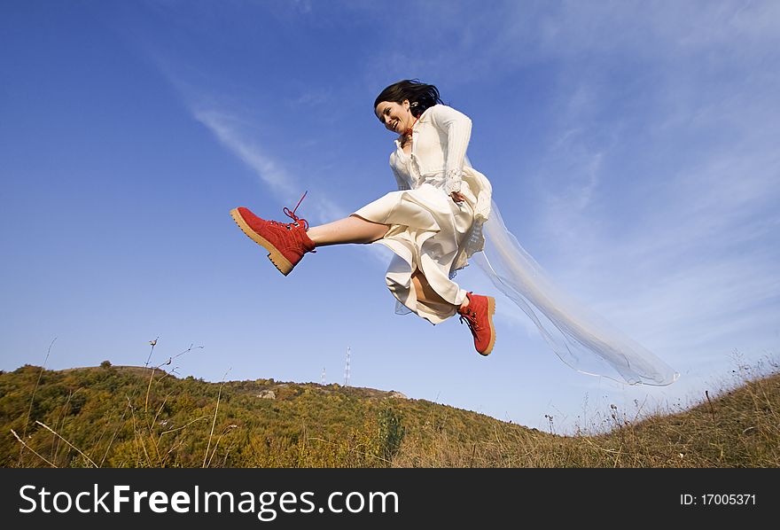 Happy bride with red boots jumping against blue sky