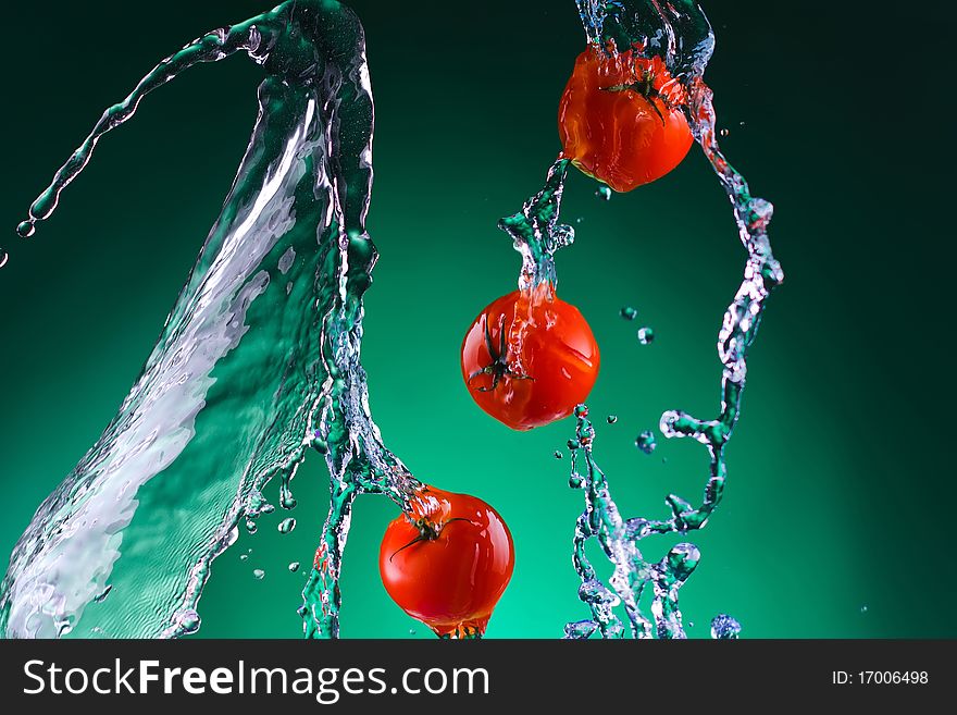 A few whole juicy bright red tomatoes in jets of water on a green background. A few whole juicy bright red tomatoes in jets of water on a green background