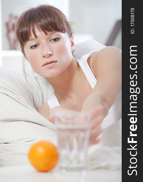 Sick woman in bed reaching for glass water on table. Sick woman in bed reaching for glass water on table