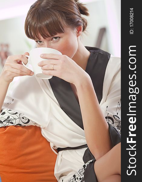 Young woman in bathrobe drinking tea at home