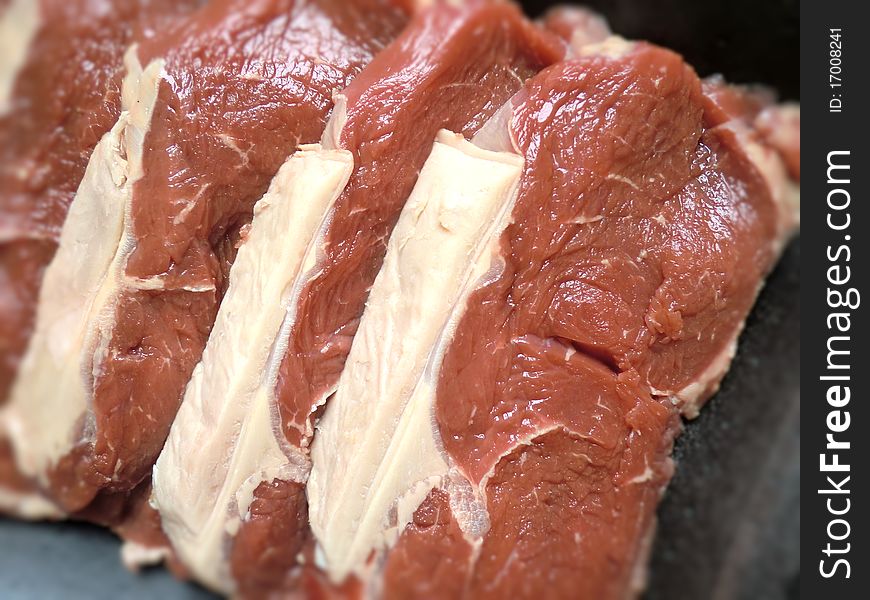 Four raw bloody beef steak slices.