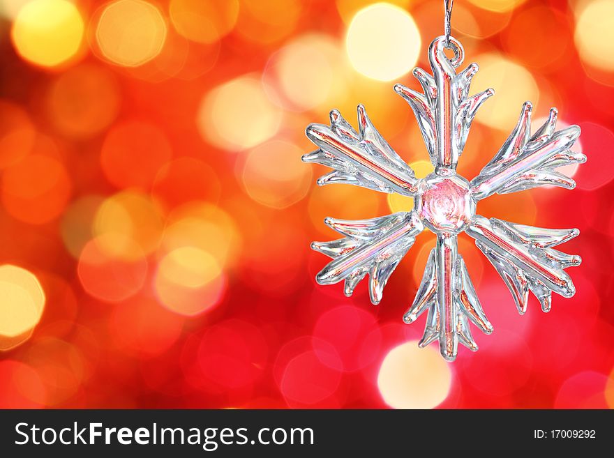 Snowflake on branch of Christmas tree against red blurred background. Snowflake on branch of Christmas tree against red blurred background