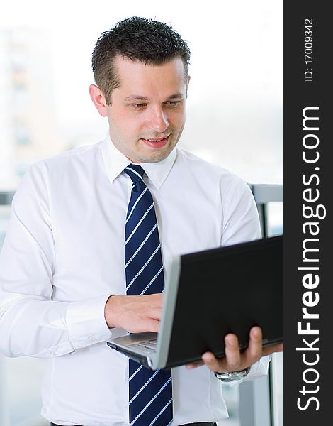 Casual looking businessman working on laptop computer in front of office window.